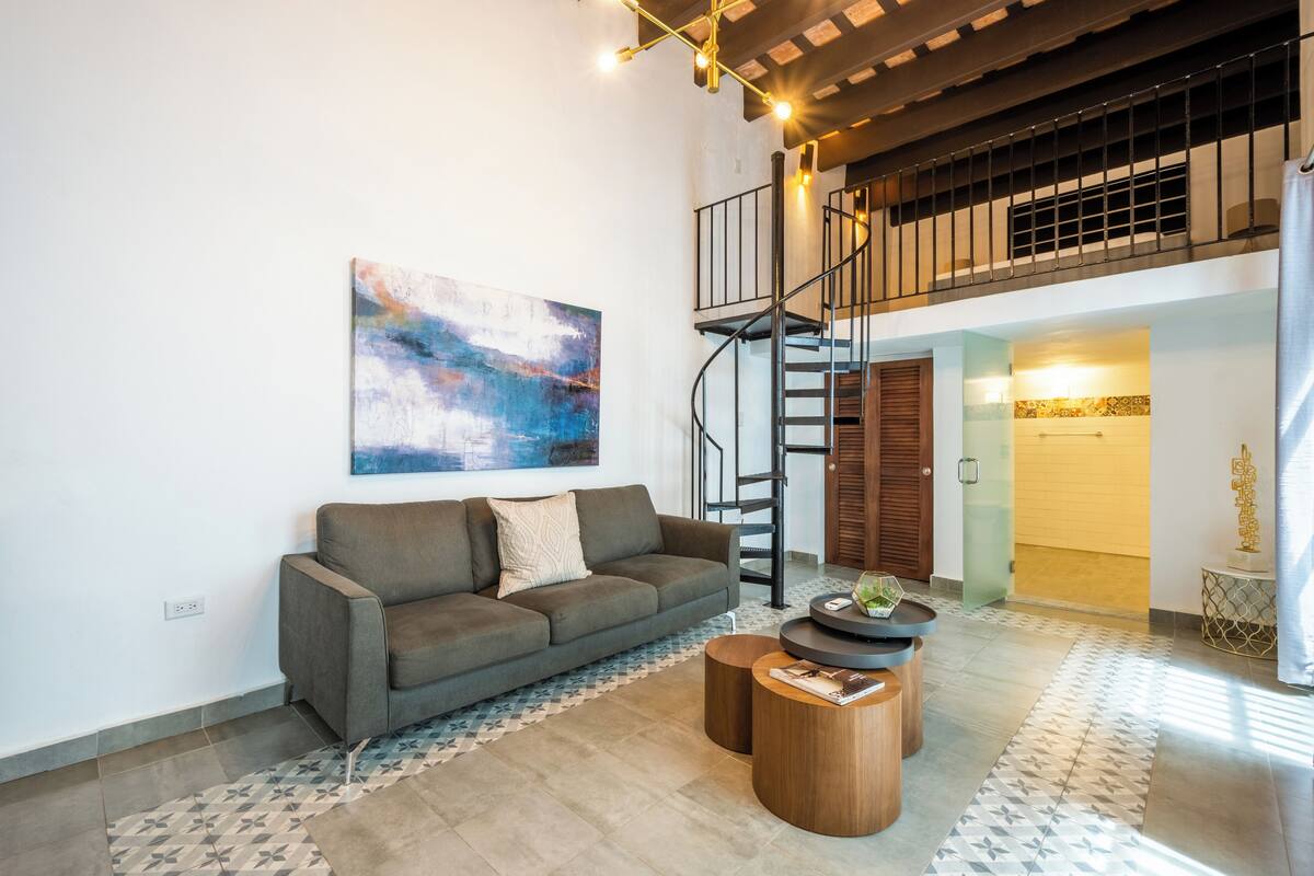 A modern living room with a grey sofa, a coffee table, and a staircase leading to an upper level.