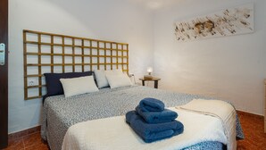 Une chambre à coucher avec une tête de lit en bois, une couvre-lit à motifs, une lampe de chevet et une œuvre d’art murale.