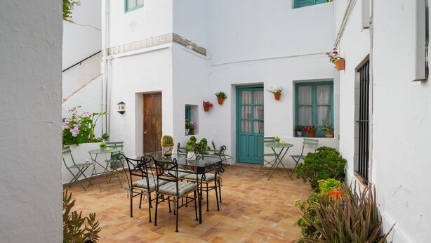 Une cour avec une table et des chaises, des plantes en pot et une porte.