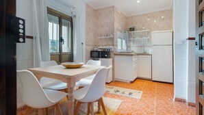 Une cuisine moderne avec un coin repas, des meubles blancs et un sol carrelé.