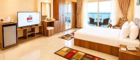 Habitación de hotel con cama, televisor, escritorio, silla, una mesita y balcón con vistas.