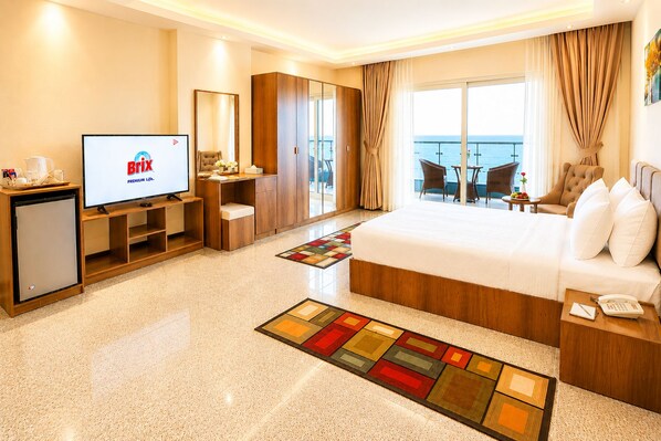 A hotel room with a bed, a TV, a desk, a chair, a small table, and a balcony with a view. - Blue Lotus Nile Suites (Aswan)