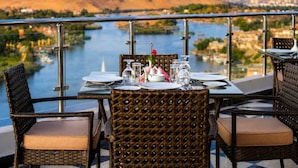A dining table set with plates, glasses, and cutlery, overlooking a river and hills.