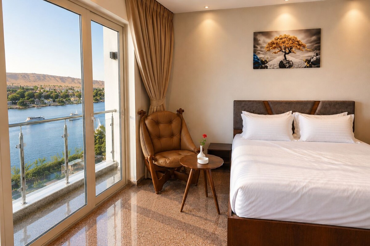 A hotel room with a large window, a bed, a chair, a small table, and a painting on the wall.