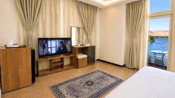 A hotel room with a large bed, a TV on a wooden stand, a desk with a chair, a small table with a chair, and a view of the sea.