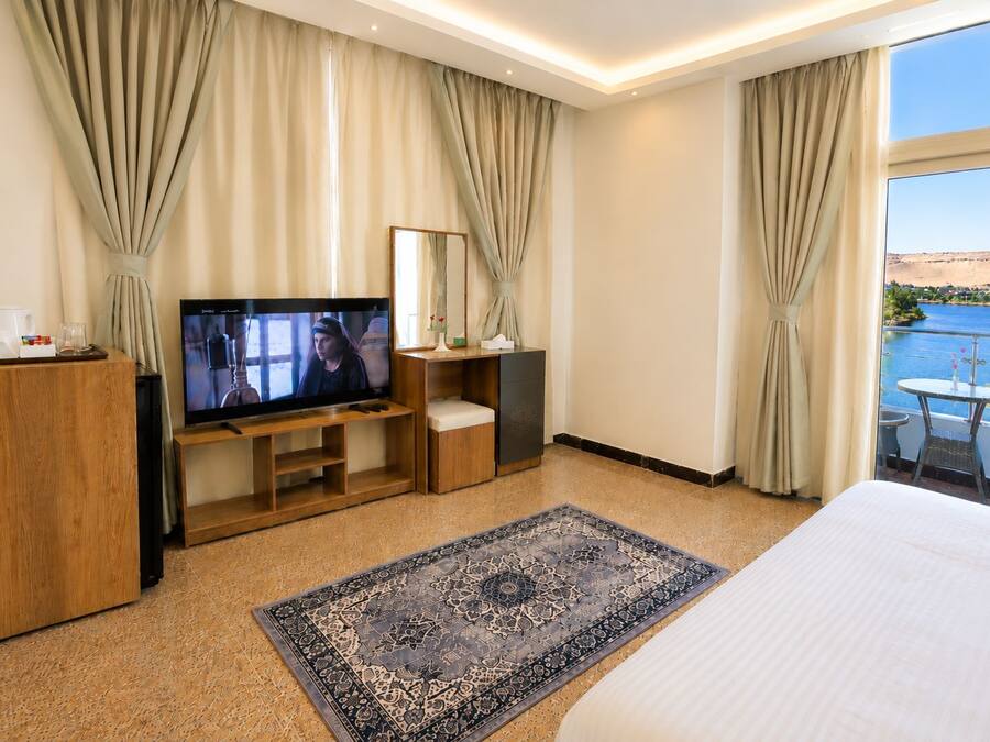 Habitación de hotel con una cama grande, un televisor sobre un mueble de madera, un escritorio con una silla, una mesita con una silla y vista al mar.