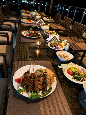 A dining area with tables set for meals, including skewered meats and rice dishes.