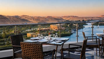 A dining area with tables set for two, overlooking a river and mountains.