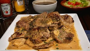 A plate of meat with sauce, condiments, and a bowl in the background.