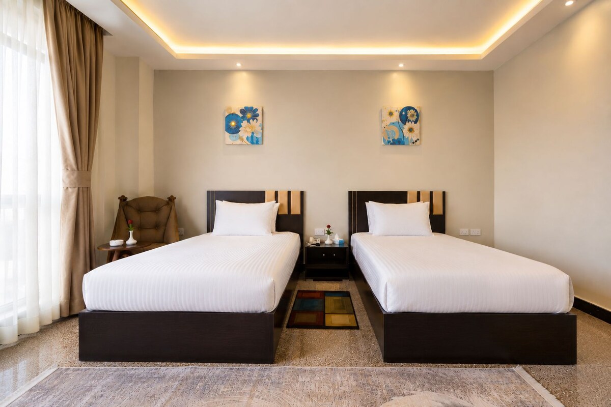 A hotel room with two beds, a chair, a small table, and artwork on the walls.