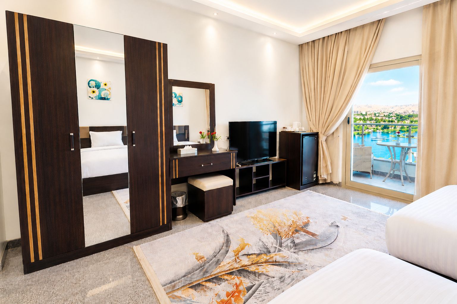 A hotel room with a bed, a TV, a minibar, a desk, a large mirror, and a balcony with a pool view.