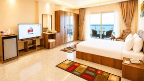 A hotel room with a bed, a TV, a desk, a chair, a small table, and a balcony with a view. - Blue Lotus Nile Suites (Aswan)