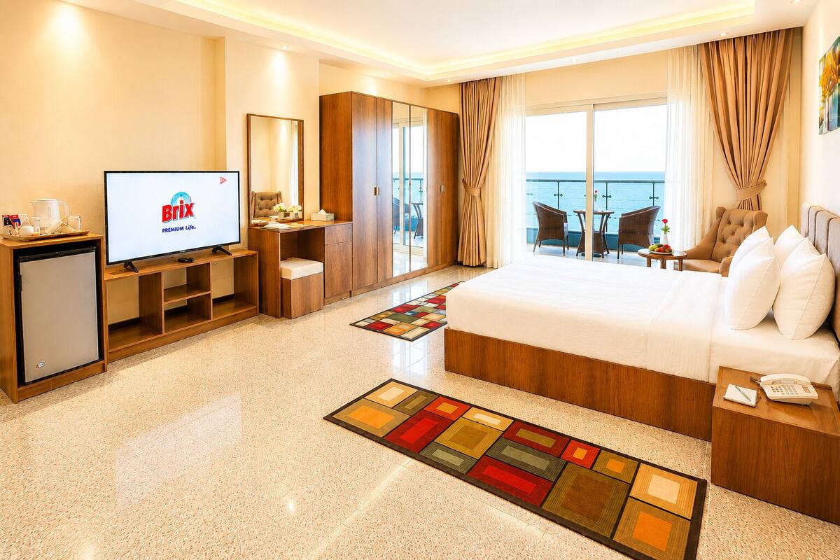 A hotel room with a bed, a TV, a desk, a chair, a small table, and a balcony with a view.