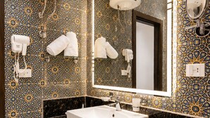 A bathroom with a white sink, a large mirror, towel hooks, and a patterned tile wall. - Blue Lotus Nile Suites (Aswan)