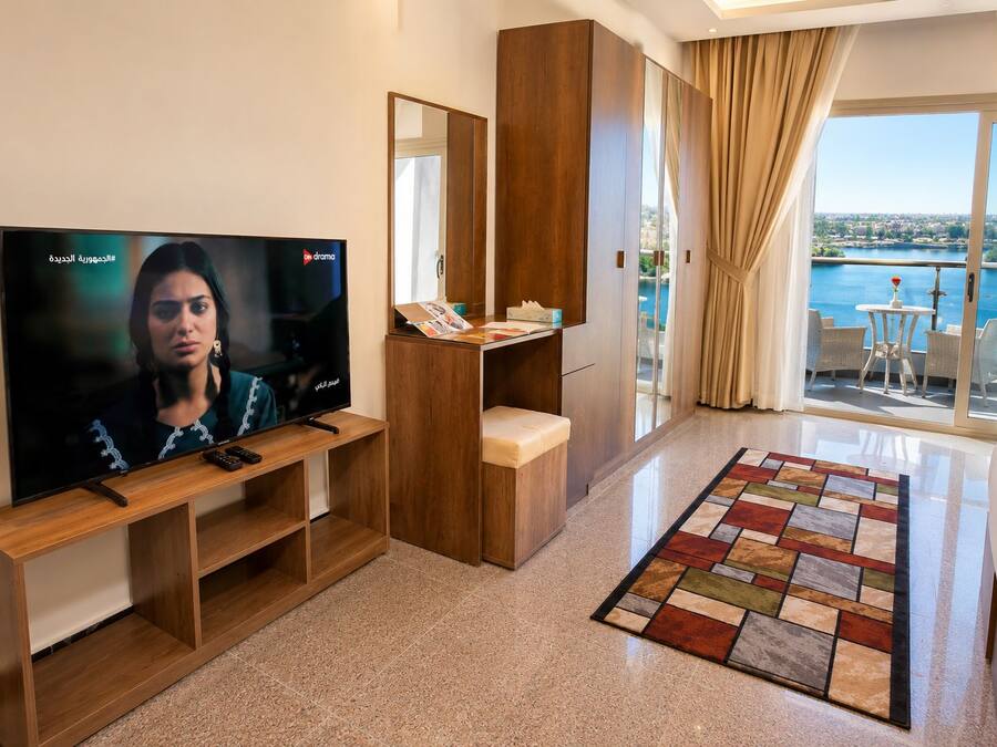 Habitación de hotel con televisor, muebles de madera, balcón con vistas y una alfombra estampada.