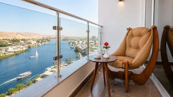 A balcony with a view of a river, a chair, a small table with a vase and a bowl, and a wall-mounted light fixture.