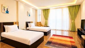 A hotel room with two beds, a TV, a desk, and a window with curtains.