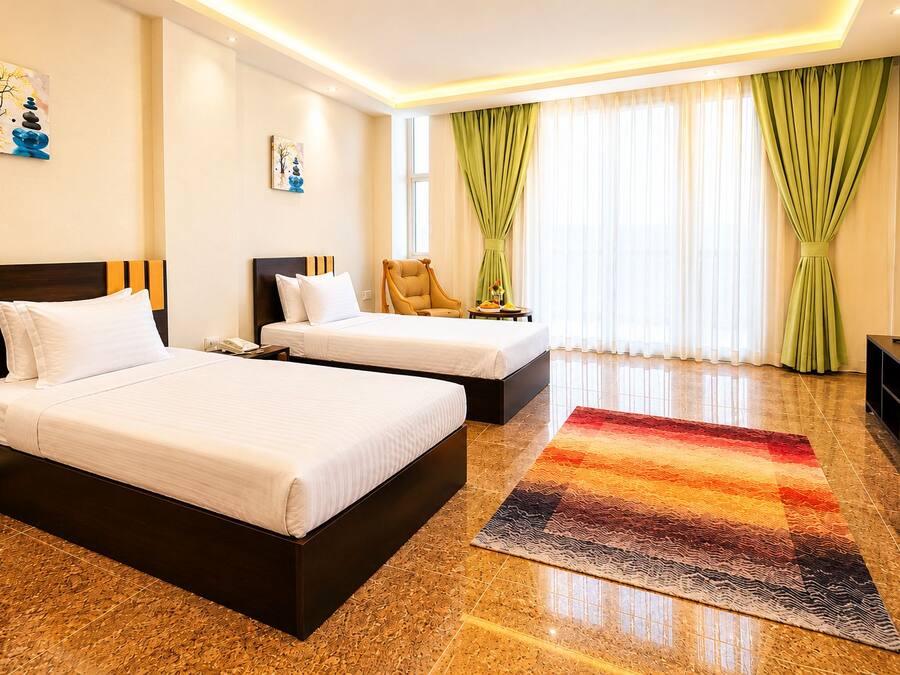 A hotel room with two beds, a TV, a desk, and a window with curtains.