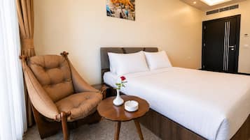 Une chambre d’hôtel avec un lit, une chaise, une petite table sur laquelle se trouve un vase, et un tableau accroché au mur.