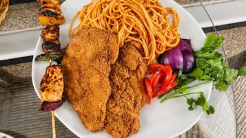 Ein Teller mit Spaghetti, paniertem Hähnchen und Gemüse.