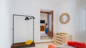 Une chambre d’hôtel avec un plancher en bois, un lit avec un oreiller rouge, une commode en bois, un miroir, un porte-vêtements et une vue sur la cuisine.