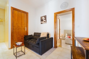 A room with a black sofa, a small table with a bowl, a wooden door, and a bed with a white headboard.