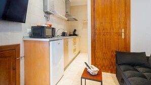 Une cuisine compacte équipée d’un four à micro-ondes, d’une cuisinière et d’un évier, avec une porte en bois et une petite table sur laquelle se trouve une télécommande.
