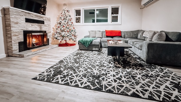 Een moderne woonkamer met een open haard, een kerstboom, een grijze bank en een getextureerd vloerkleed.