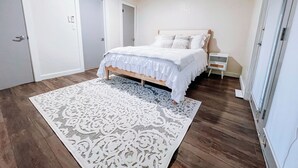 Een slaapkamer met een bed, een wit kleed, houten vloeren en een plafondventilator.