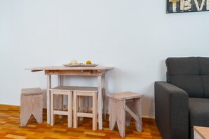 Une petite table en bois avec des tabourets, un canapé gris et un mur sur lequel on peut apercevoir une partie du mot « TEV ».