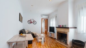 A living room with a sofa, a coffee table, a fireplace, a television, and a bicycle mounted on the wall. - Apartment 'Lolita' with Shared Garden, Wi-Fi and Air Conditioning (Carmona)