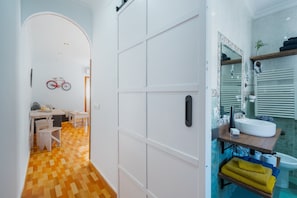 A hallway leading to a room with a bicycle mounted on the wall, a wooden dining table, and a white door.