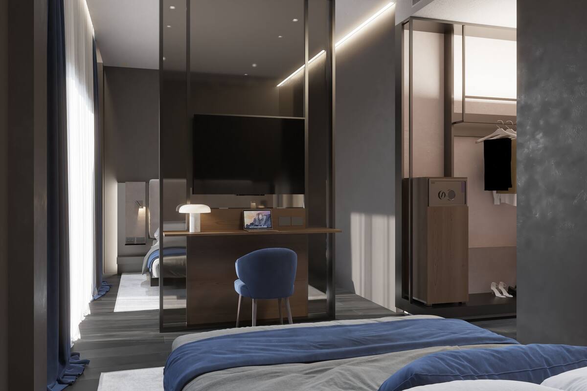 A modern hotel room with a large bed, a desk with a laptop, a chair, and a wardrobe.