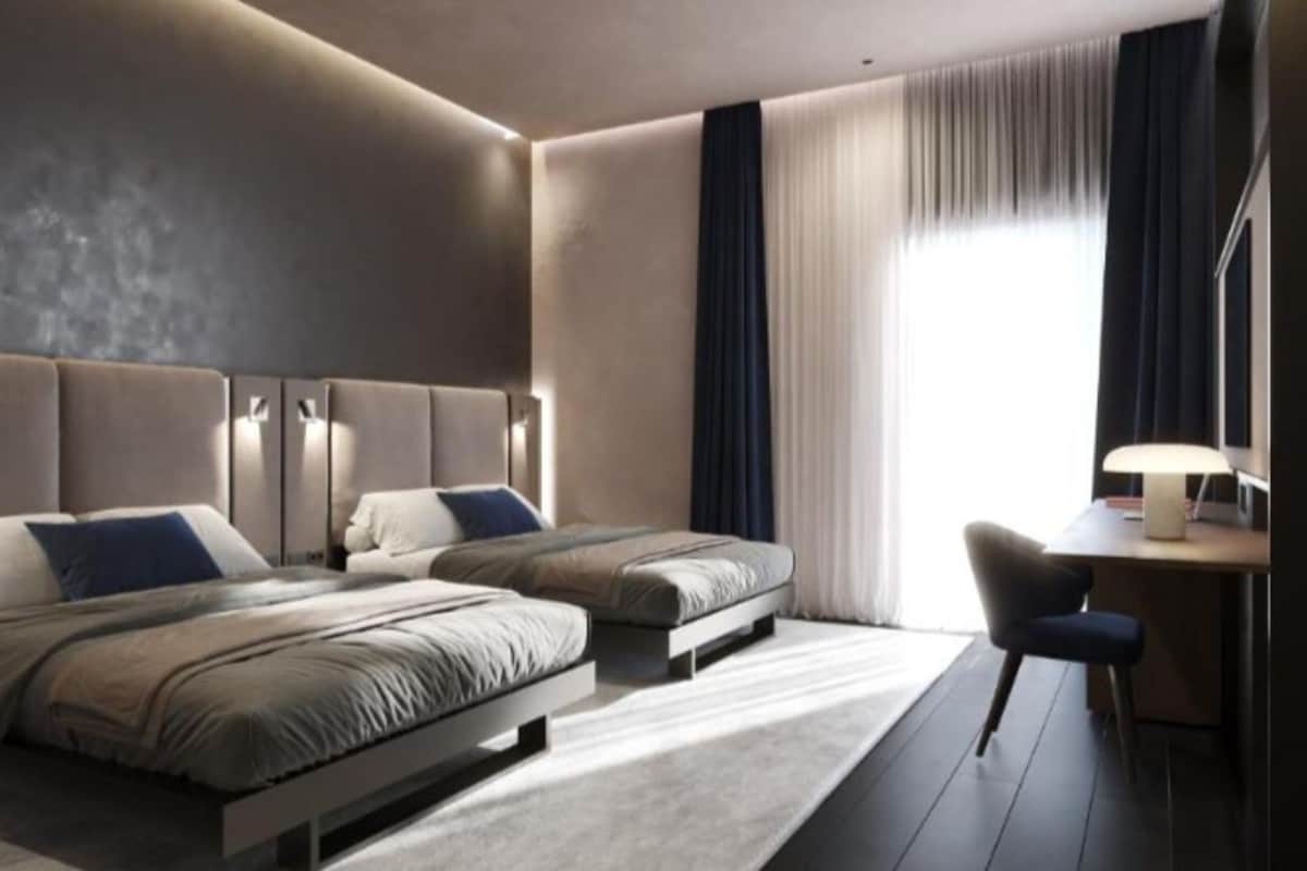 A modern hotel room with two beds, a desk, and a chair.