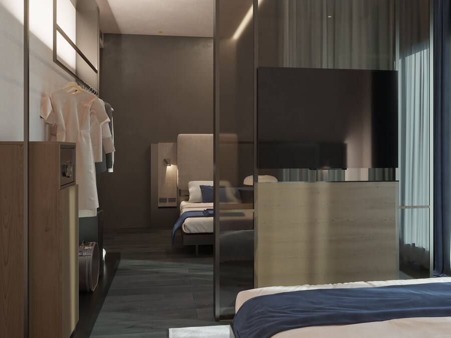 A modern hotel room with a bed, a desk, a wardrobe, and a large mirror.