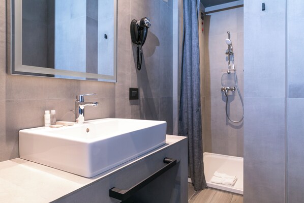 Une salle de bain moderne équipée d’un grand lavabo, d’un sèche-cheveux, d’une douche et d’un miroir.