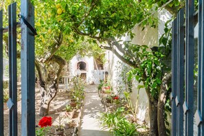 A narrow garden pathway flanked by potted plants and trees, leading to a white building with an arched entrance. - Apartment 'Vittorio Stella' with Sea View, Private Terrace and Air Conditioning (Valderice)