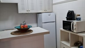 Eine Küche mit weißen Schränken, einem weißen Kühlschrank, einer Mikrowelle und einer Obstschale auf der Arbeitsplatte.