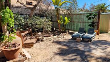 A backyard with a wooden deck, potted plants, a green fence, and two lounge chairs.