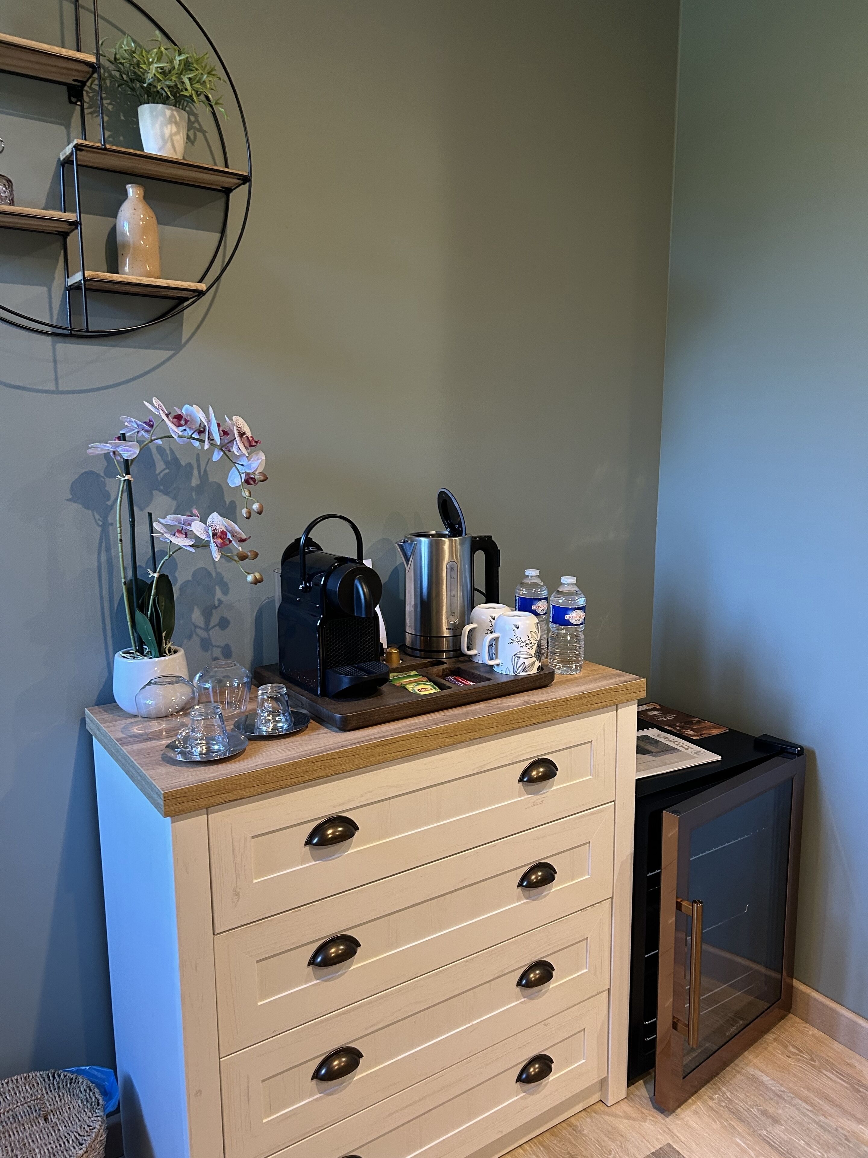A kitchenette with a coffee maker, kettle, and tea set on the counter.