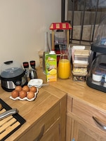 A kitchen counter with a juicer, eggs, a carton of juice, and various kitchen utensils.