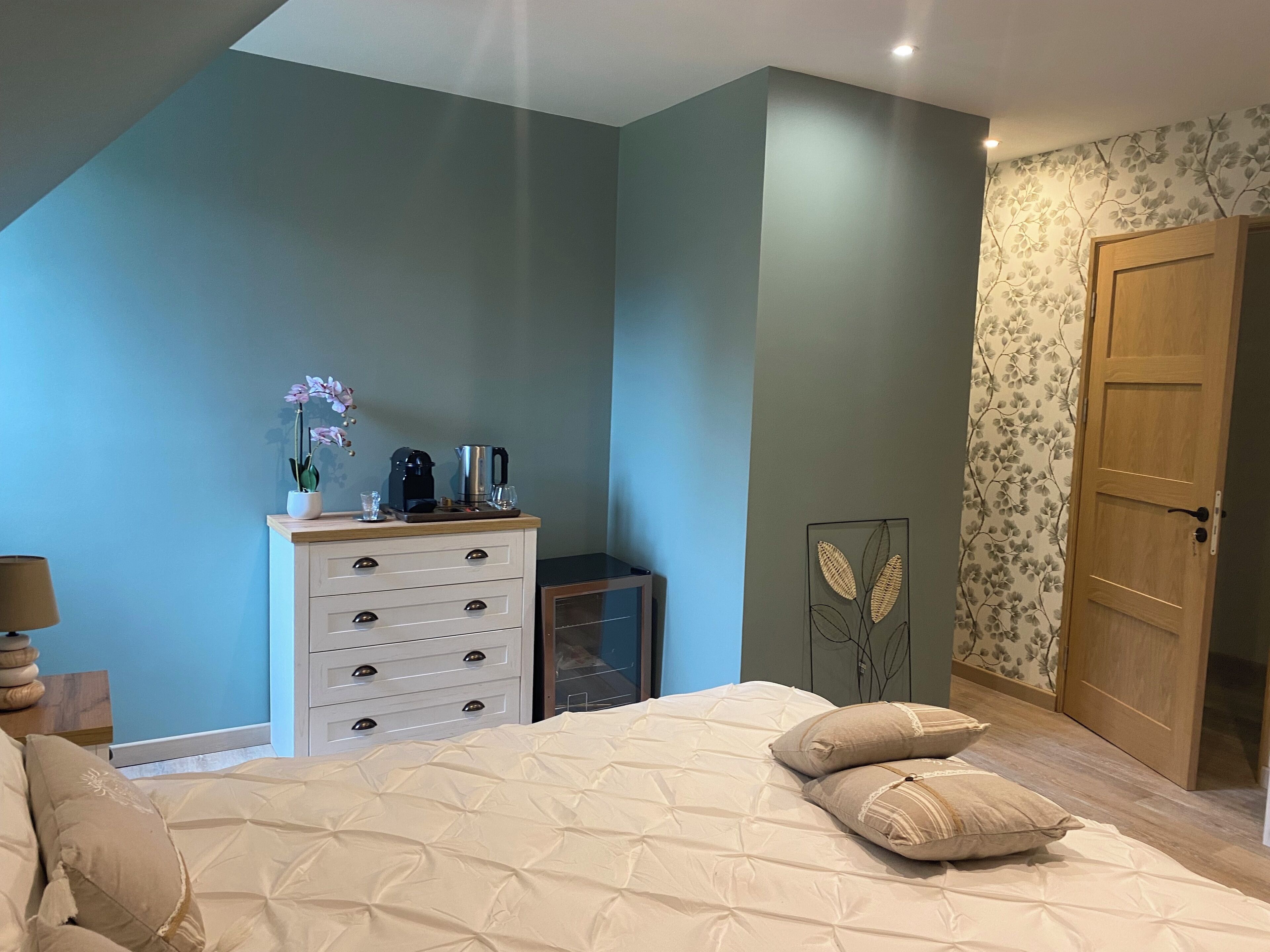 A bedroom with a bed, a dresser, a coffee maker, and a door.