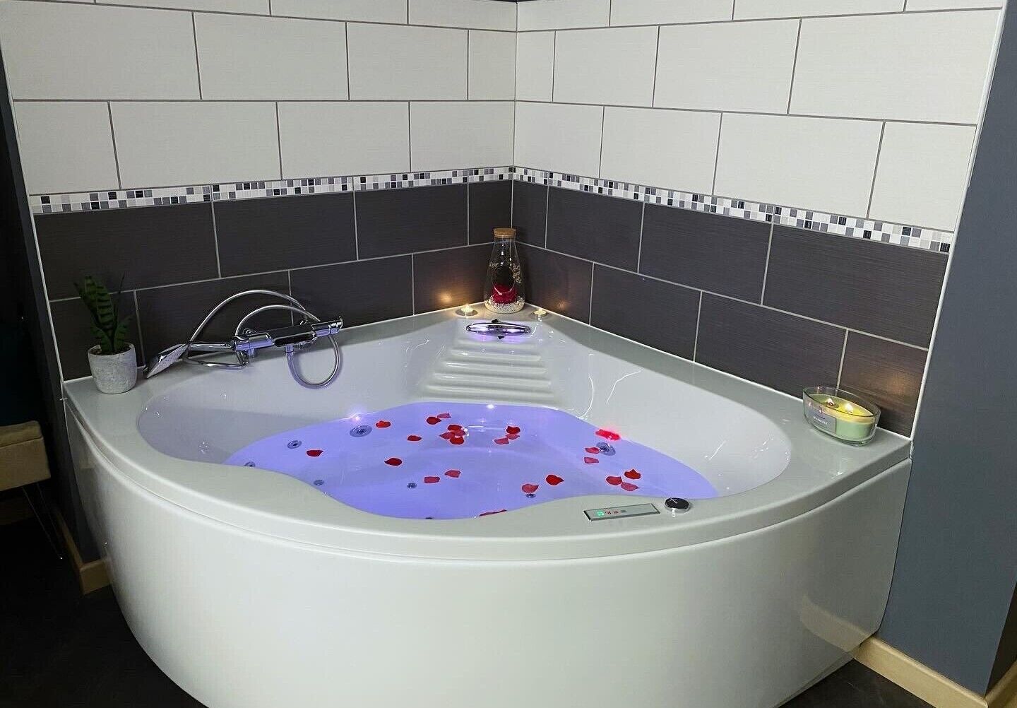 Un baño moderno con una bañera independiente, una pequeña planta en maceta y una vela al borde.