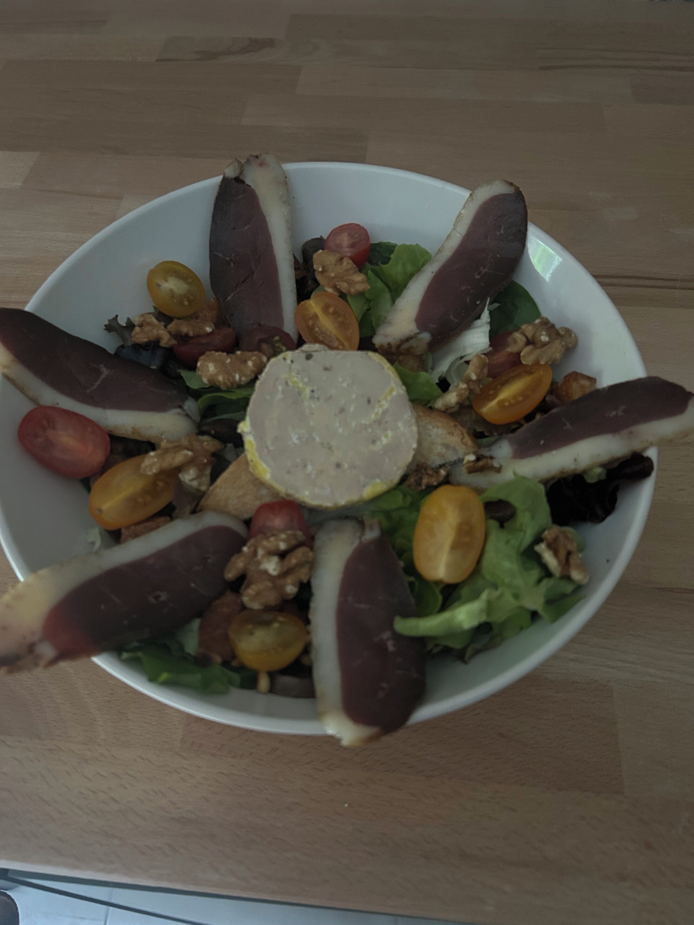 Un tazón blanco con una ensalada de lechuga, tomates cherry, nueces y rodajas de berenjena morada.