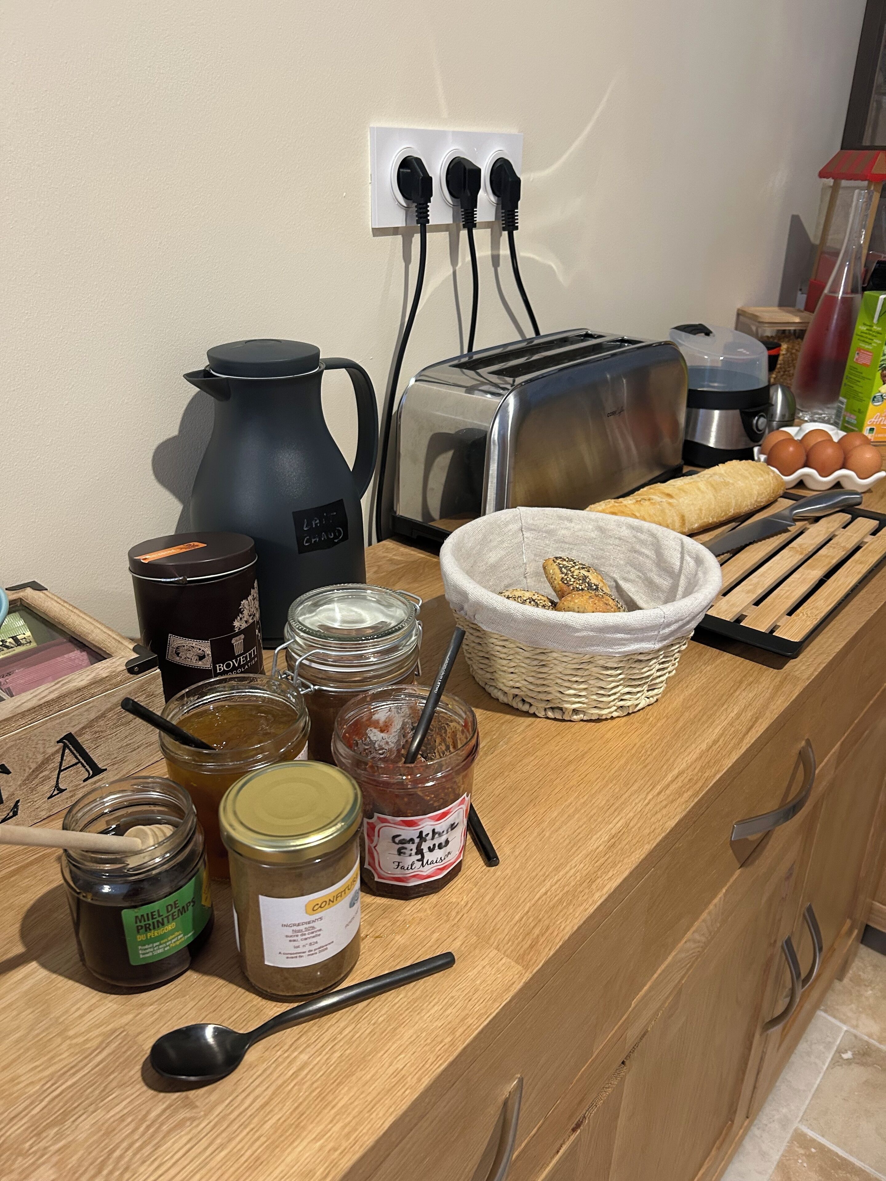 Una encimera de cocina con diferentes alimentos, un tostador, una cafetera y una cesta de pan.