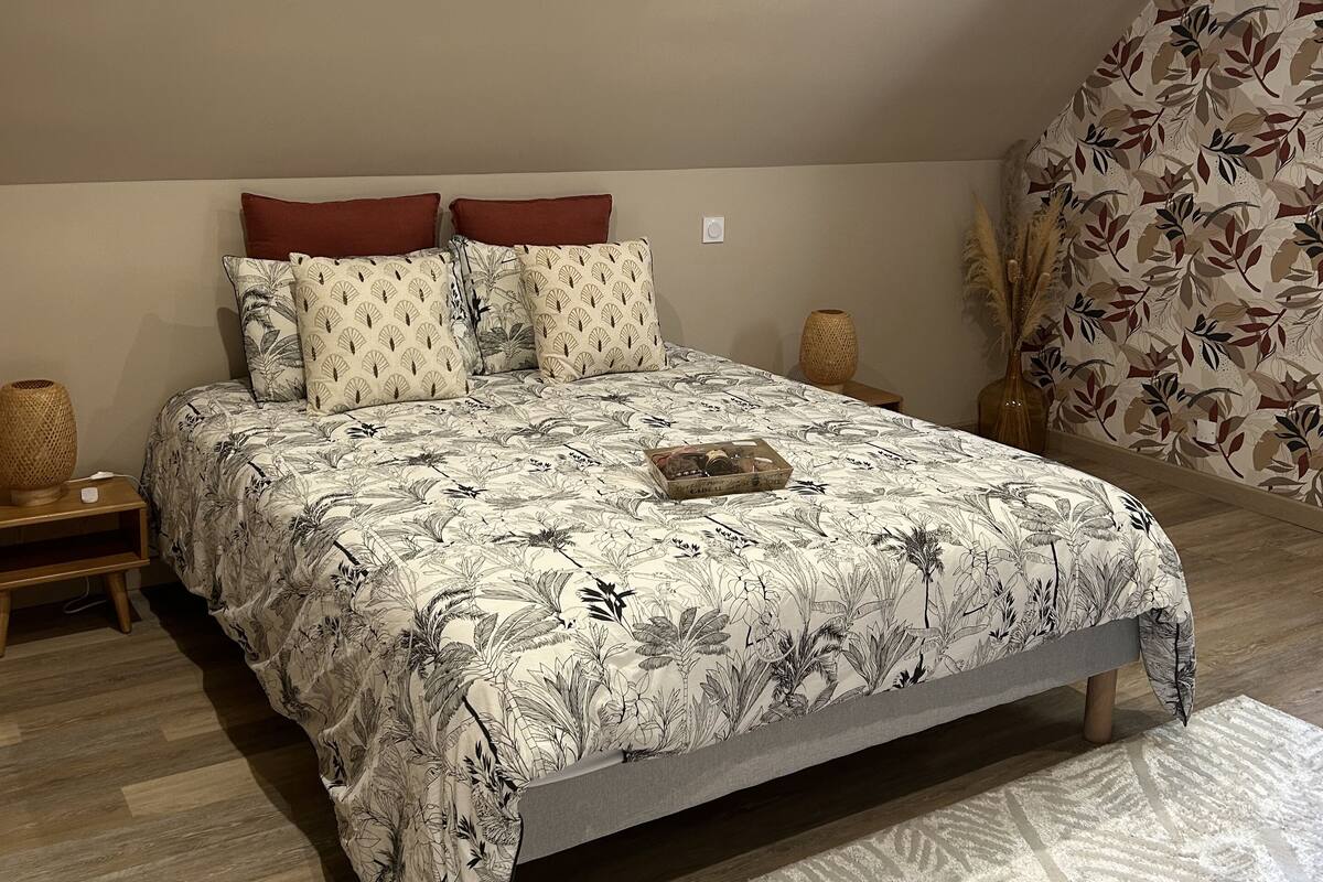 A bedroom with a large bed, a nightstand, a decorative vase, and a patterned wall.