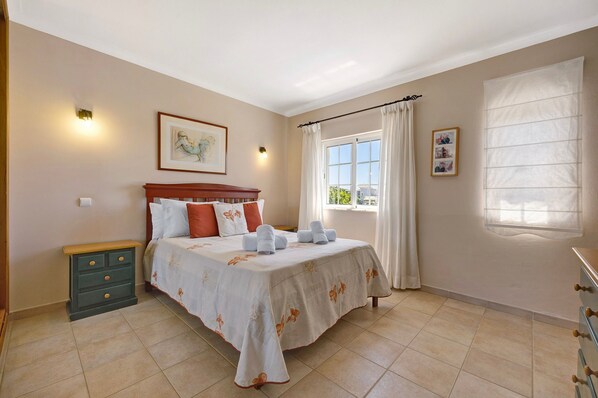A bedroom with a bed, a nightstand, a window with curtains, and a wall-mounted light.