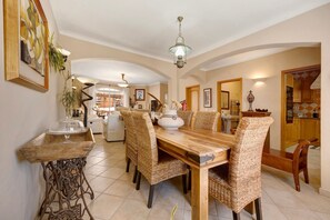 A dining area with a wooden table and wicker chairs, a decorative vase, and a hanging light fixture.