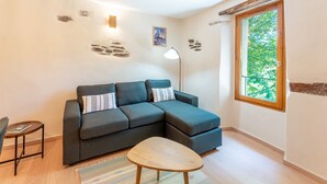 Een moderne woonkamer met een hoekbank, een klein houten tafeltje en een groot raam met uitzicht op groen.