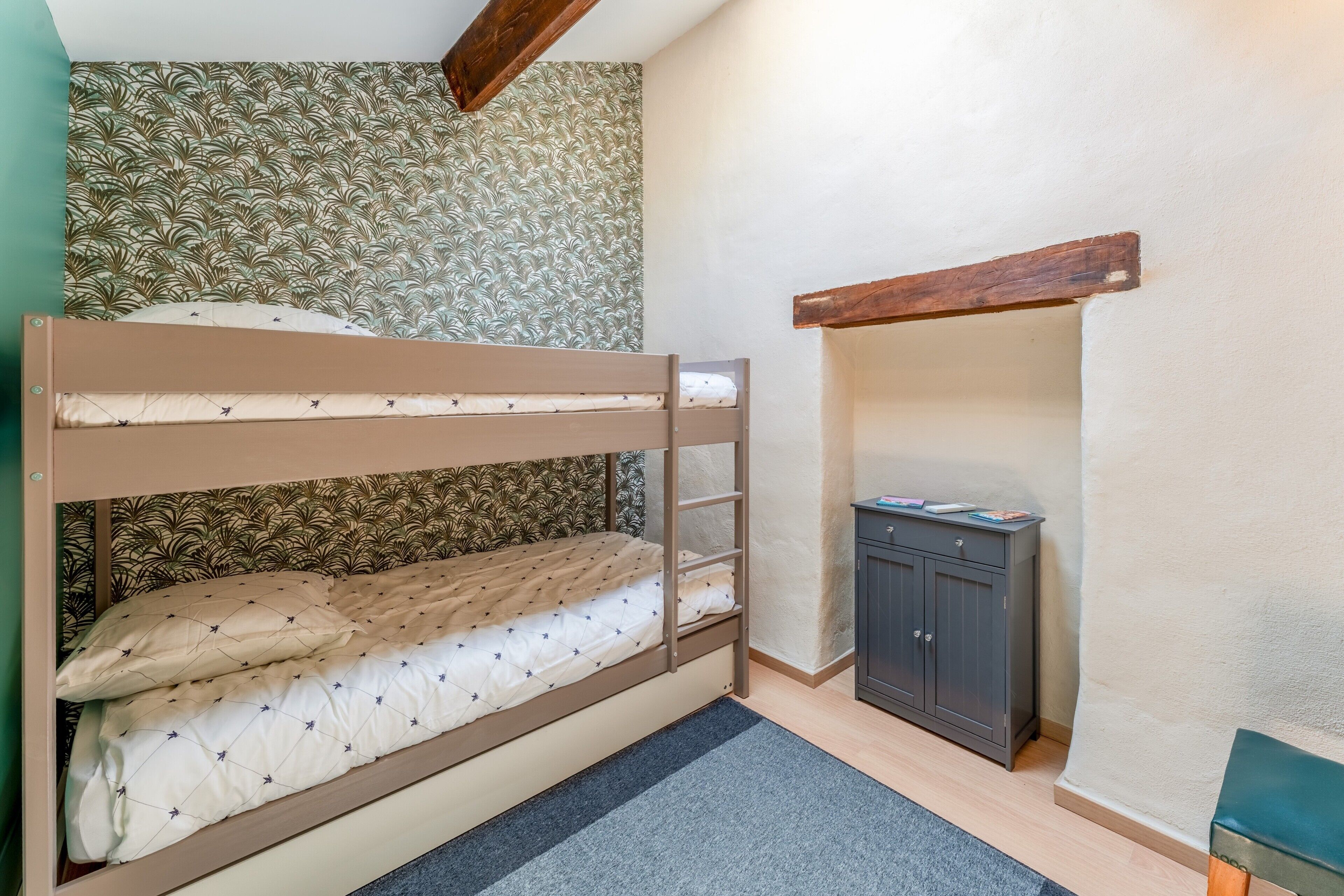 Un lit superposé avec une structure en bois, une petite armoire et un papier peint à motifs.